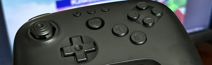 Close-up of a black game controller showing the left analog stick, D-pad, and A/B buttons with a Start button visible.